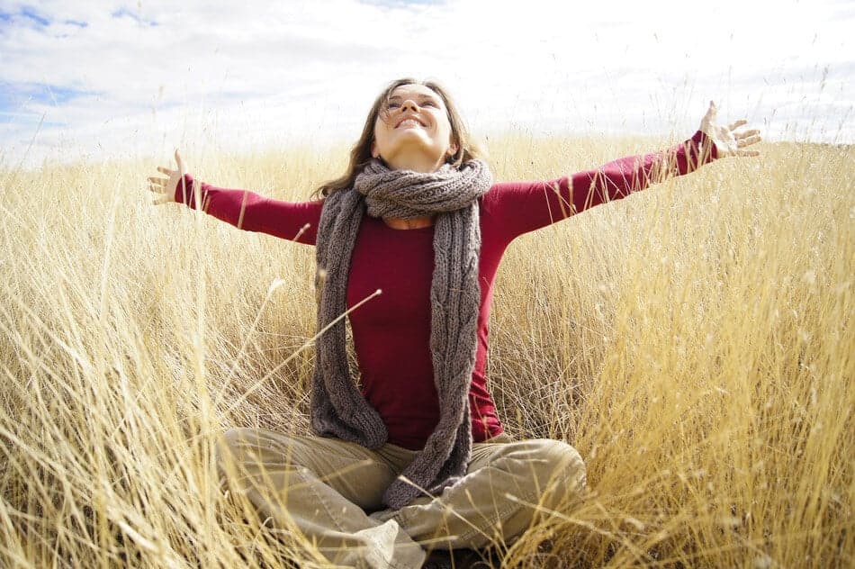 Beautiful young woman enjoying sunshine in a field with long grass